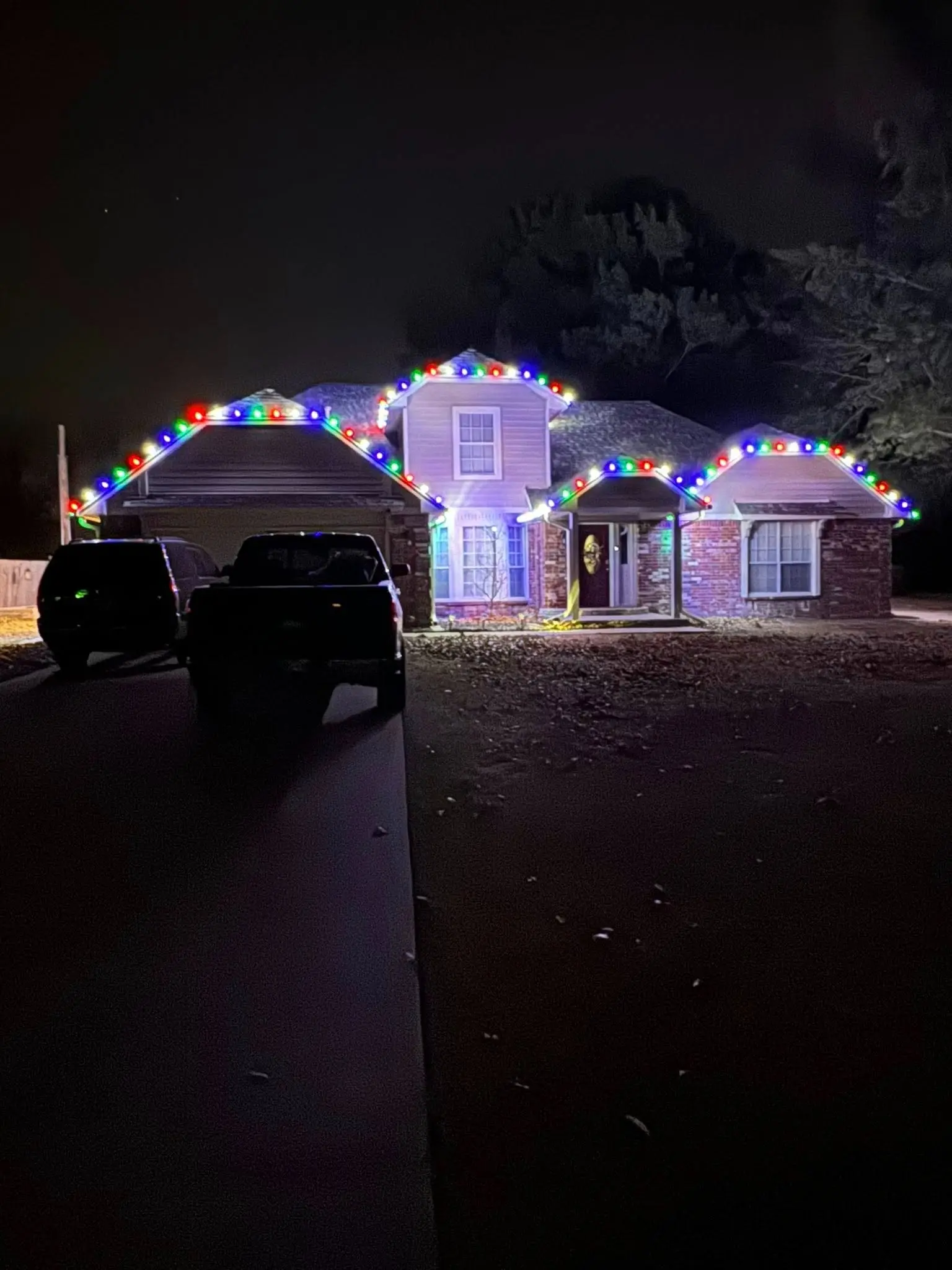 Two-story home at night with multicolor Christmas roofline lights installed by Firehouse Custom Lighting